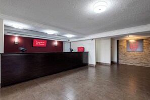Aula, jossa on tumma vastaanottotiski, kaksi kylttiä, joista ilmenee, että kaikissa huoneissa on käytettävissä ilmainen Wi-Fi, ja seinällä Red Roof Inn -hotellin kyltti.