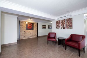 Een lobby met een Red Roof Inn bord, een stenen muur, een houten vloer, twee leren fauteuils en drie ingelijste kunstwerken.