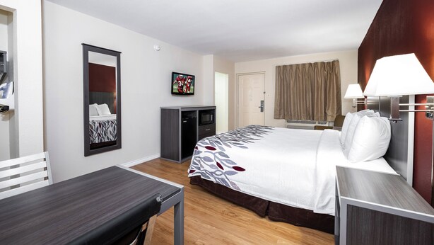 A hotel room with a bed, a desk, a mirror, a television, and a door.