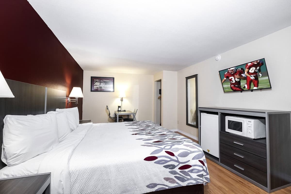 A hotel room with a bed, a desk, a chair, a microwave, and a TV on the wall.