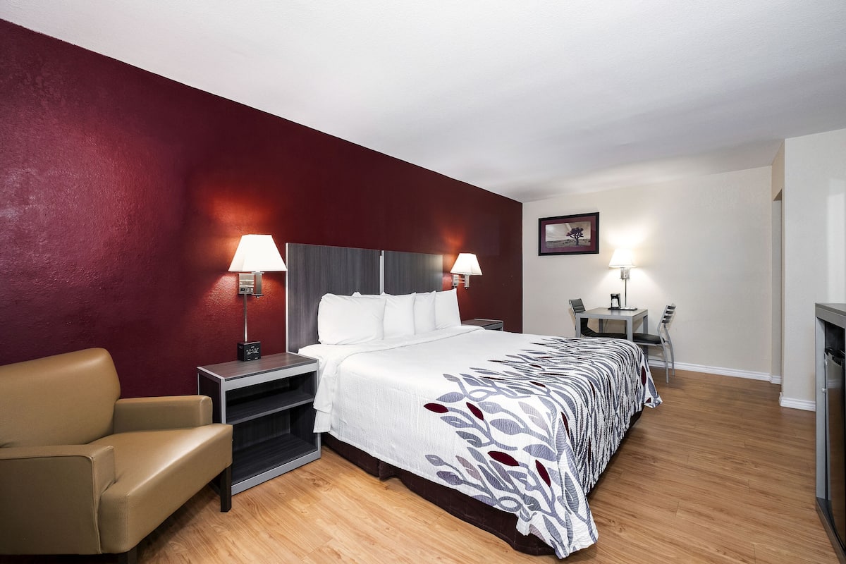 A hotel room with a bed, two bedside lamps, a chair, a desk, and a TV.
