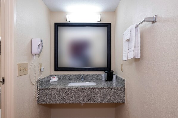 A bathroom with a granite countertop, a sink, a mirror, a towel rack with towels, a hairdryer, and a phone.