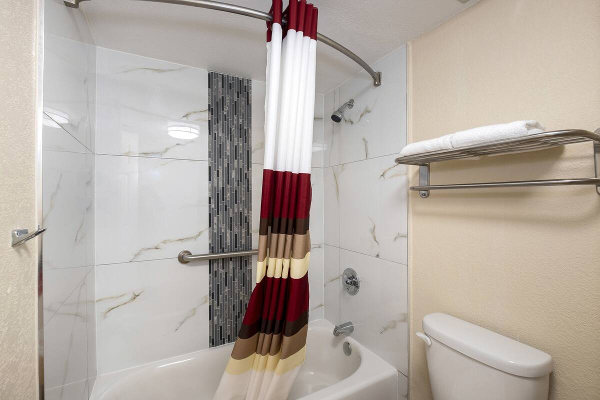 Een badkamer met douchegordijn, bad, toilet en handdoekhouder.