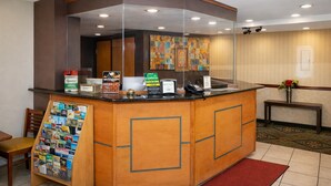 A reception area with a wooden counter, a glass display case with brochures, a phone, and a small desk with a vase of flowers. - Knights Inn Gallup at 3208 W Hwy 66 (Gallup)