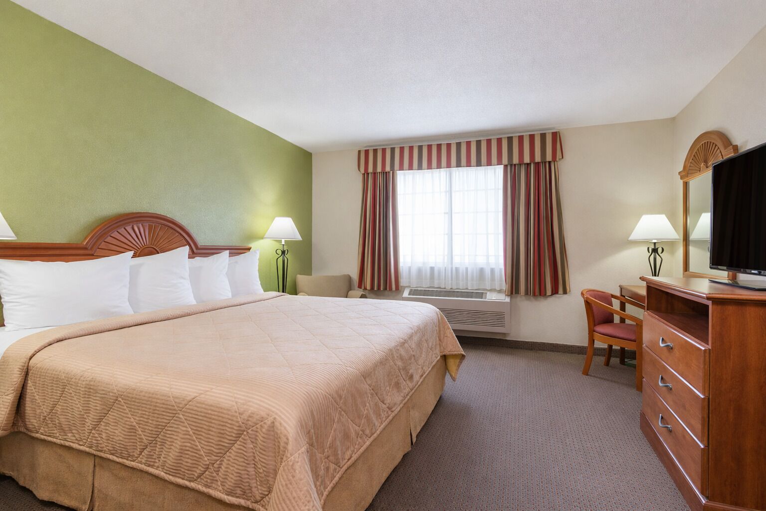 A hotel room with a large bed, a desk with a chair, a television, and a window with curtains.