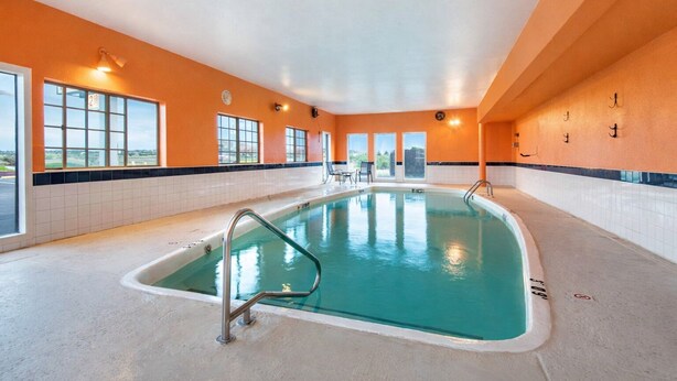 An indoor swimming pool with clear glass walls, a tiled floor, and a view of the outdoors through large windows. - Knights Inn Gallup at 3208 W Hwy 66 (Gallup)