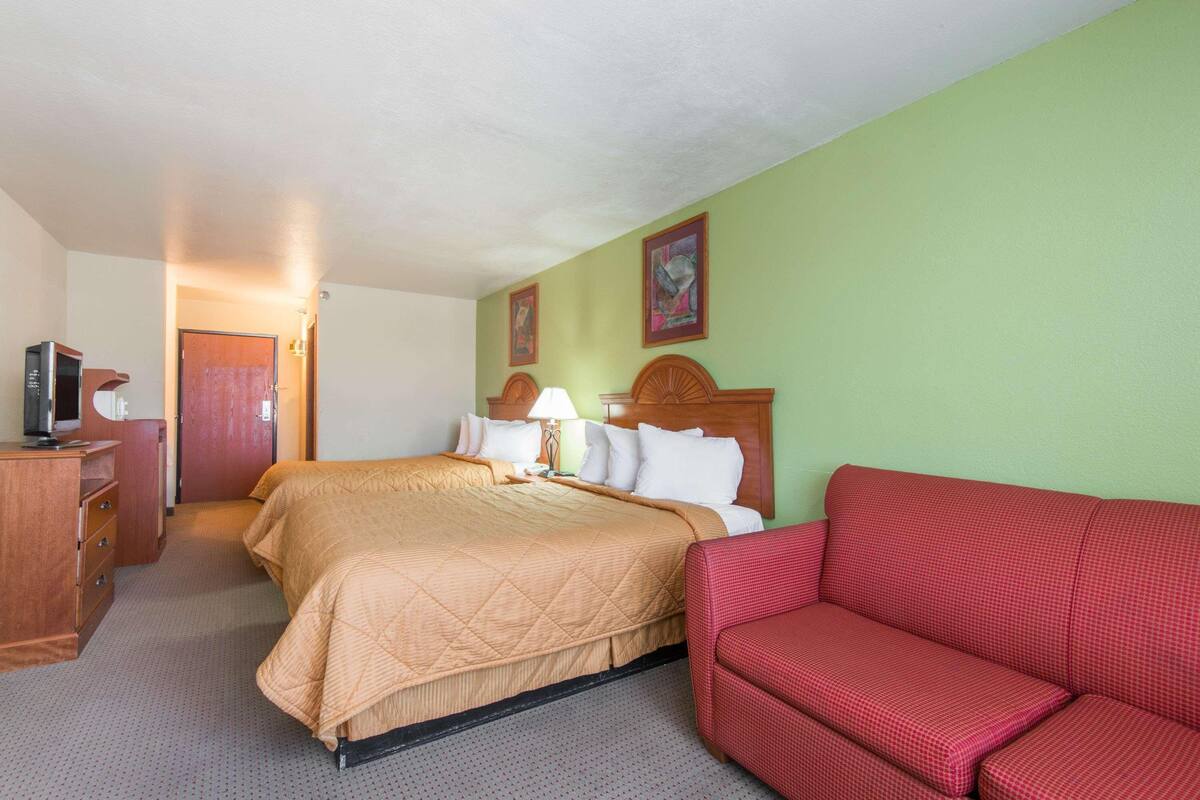 A hotel room with a bed, a red couch, a wooden dresser, and a television.