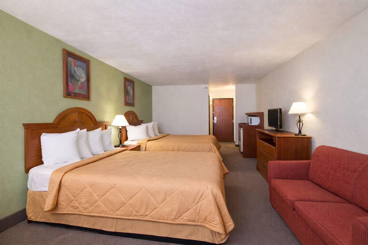 A hotel room with two beds, a television, a desk, and a red sofa.