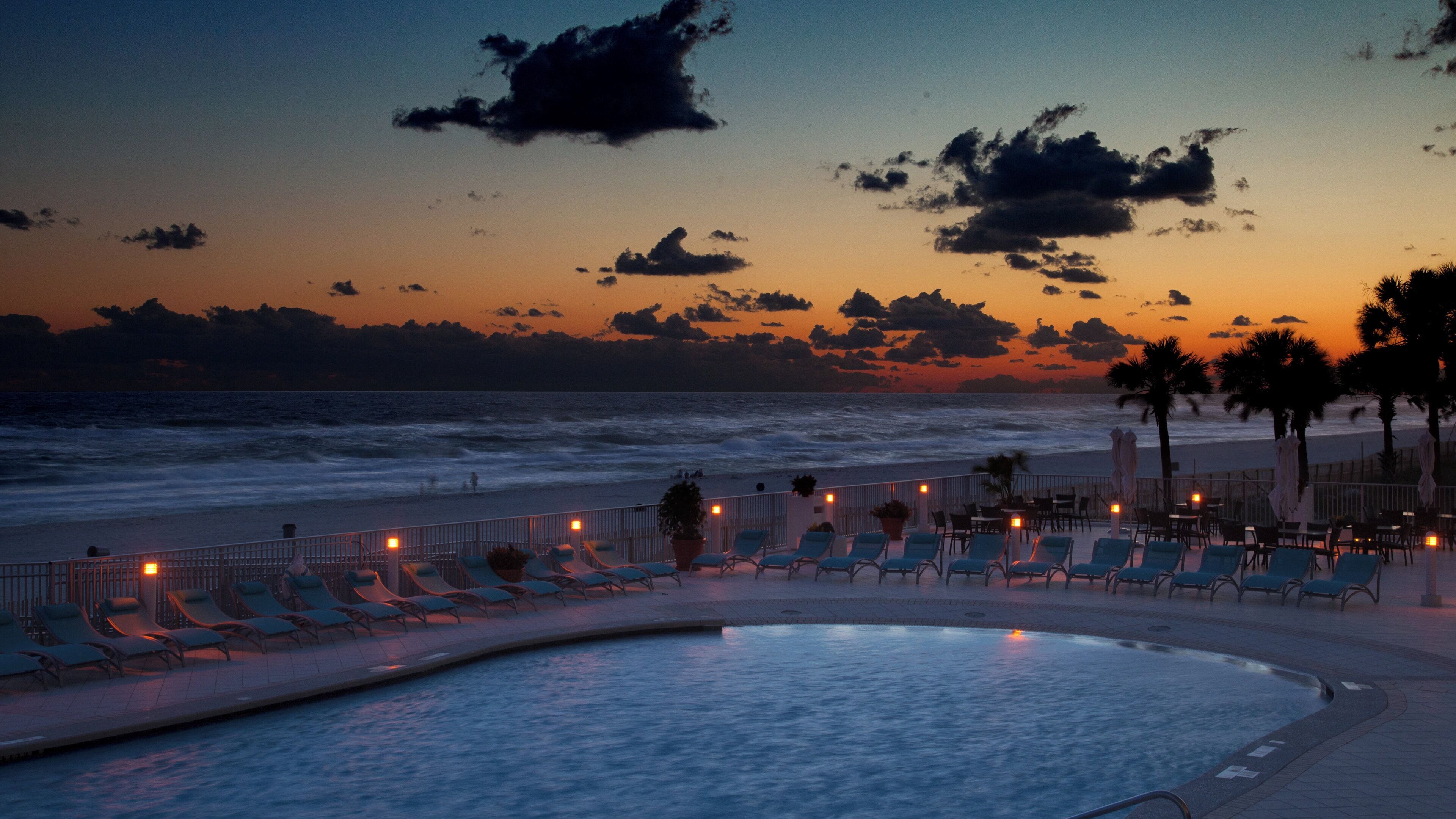 Zona de piscina con sillones de descanso y vista al océano al atardecer.