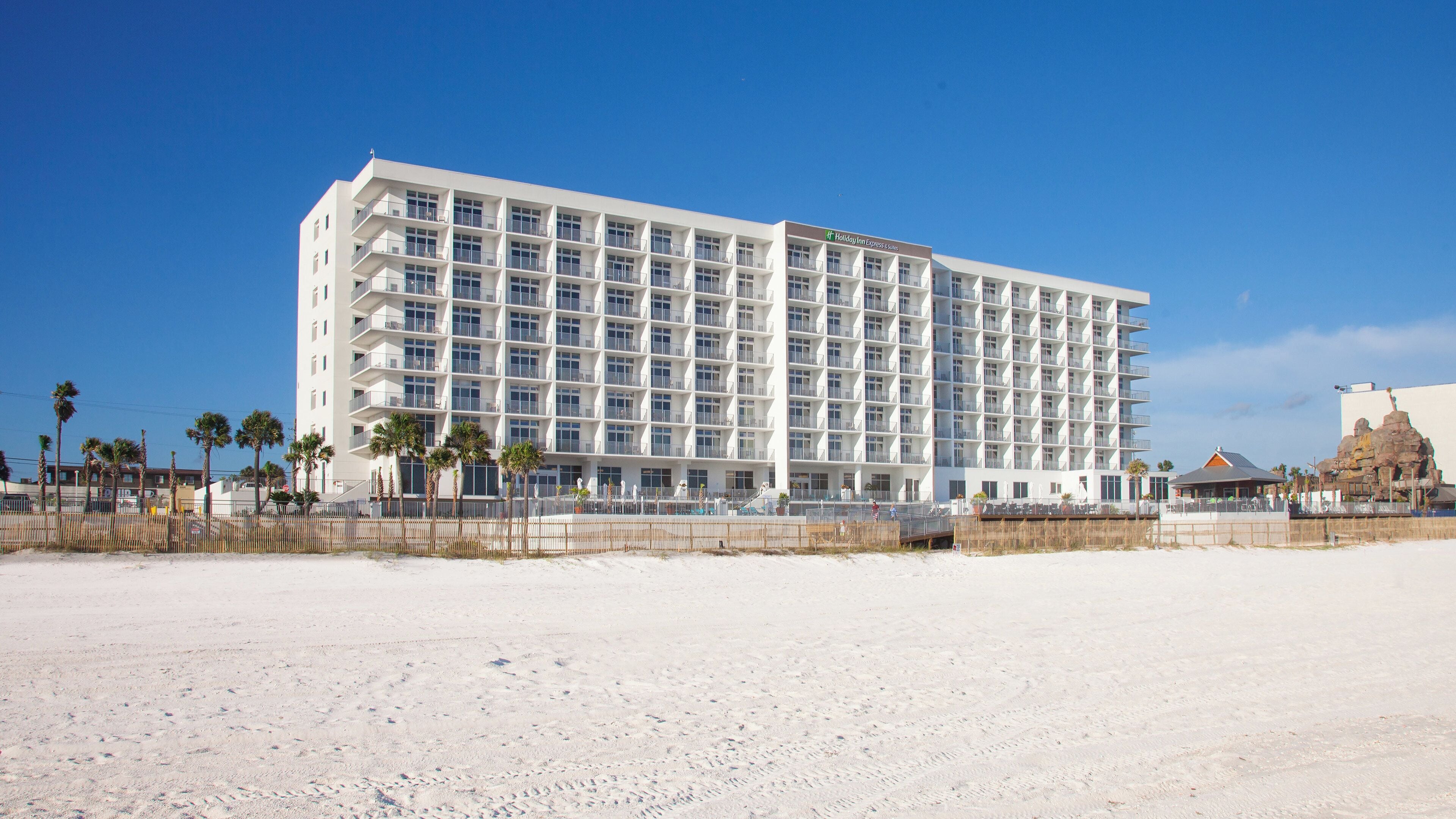 A large, multi-story hotel with balconies, located on a sandy beach.