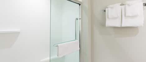 Um banheiro moderno com box de vidro, parede revestida de azulejos brancos e porta-toalhas com toalhas dobradas.