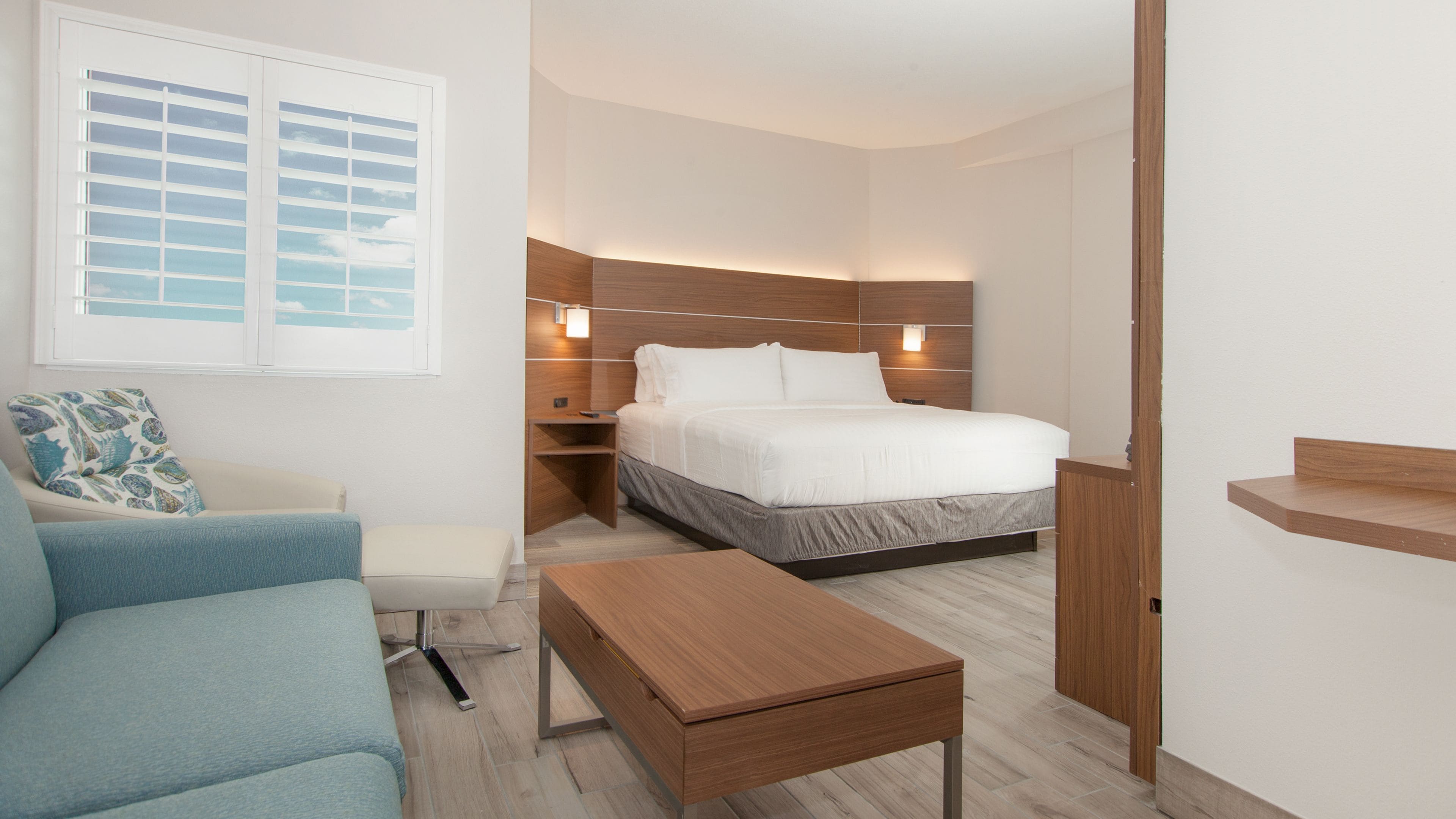 A modern hotel room with a bed, a sofa, a wooden coffee table, and a nightstand.