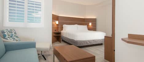A modern hotel room with a bed, a sofa, a wooden coffee table, and a nightstand.