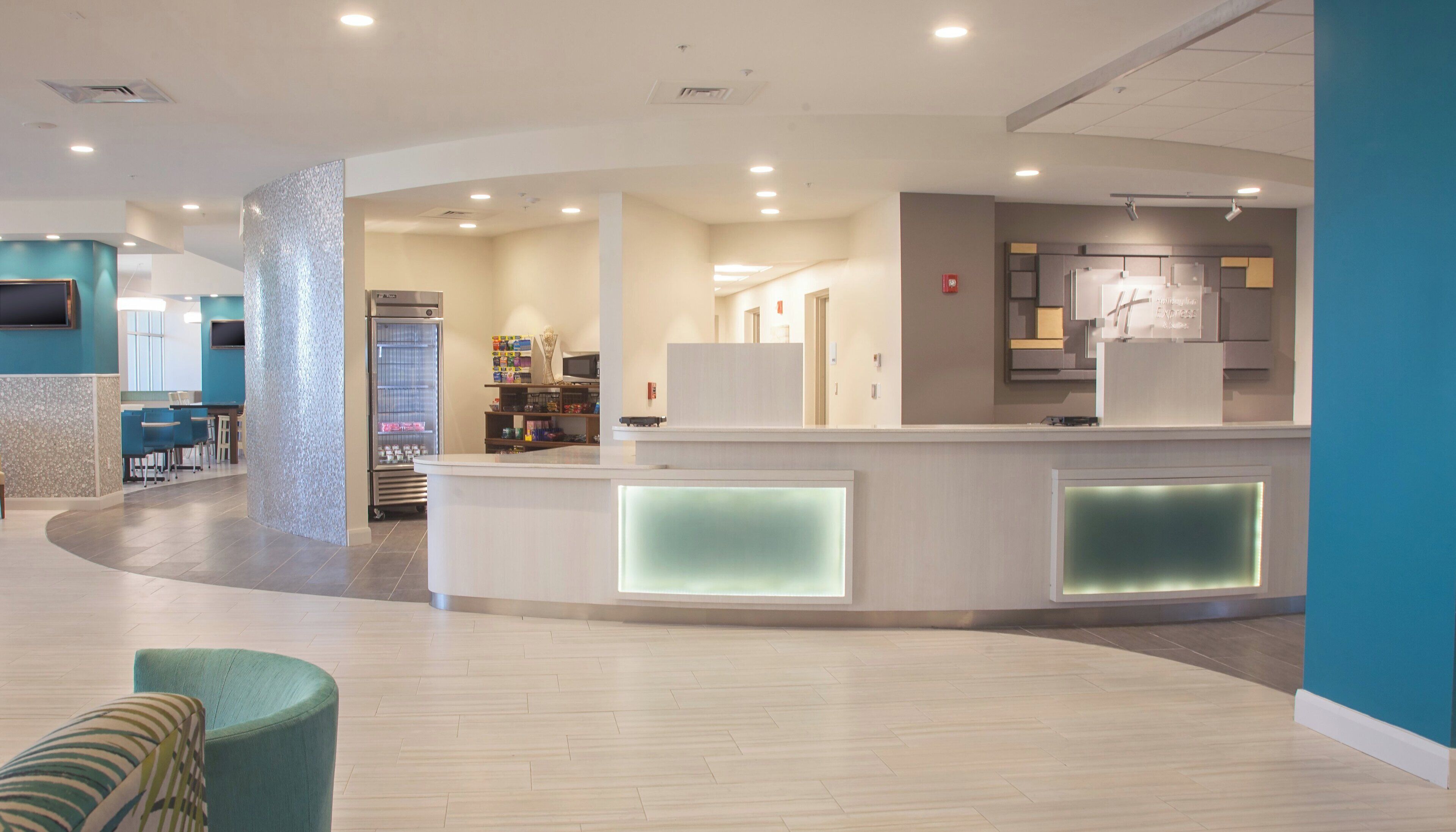 A modern reception area with a curved counter, a refrigerator, and a seating area with a teal armchair.