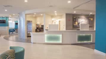 A modern reception area with a curved counter, a refrigerator, and a seating area with a teal armchair.
