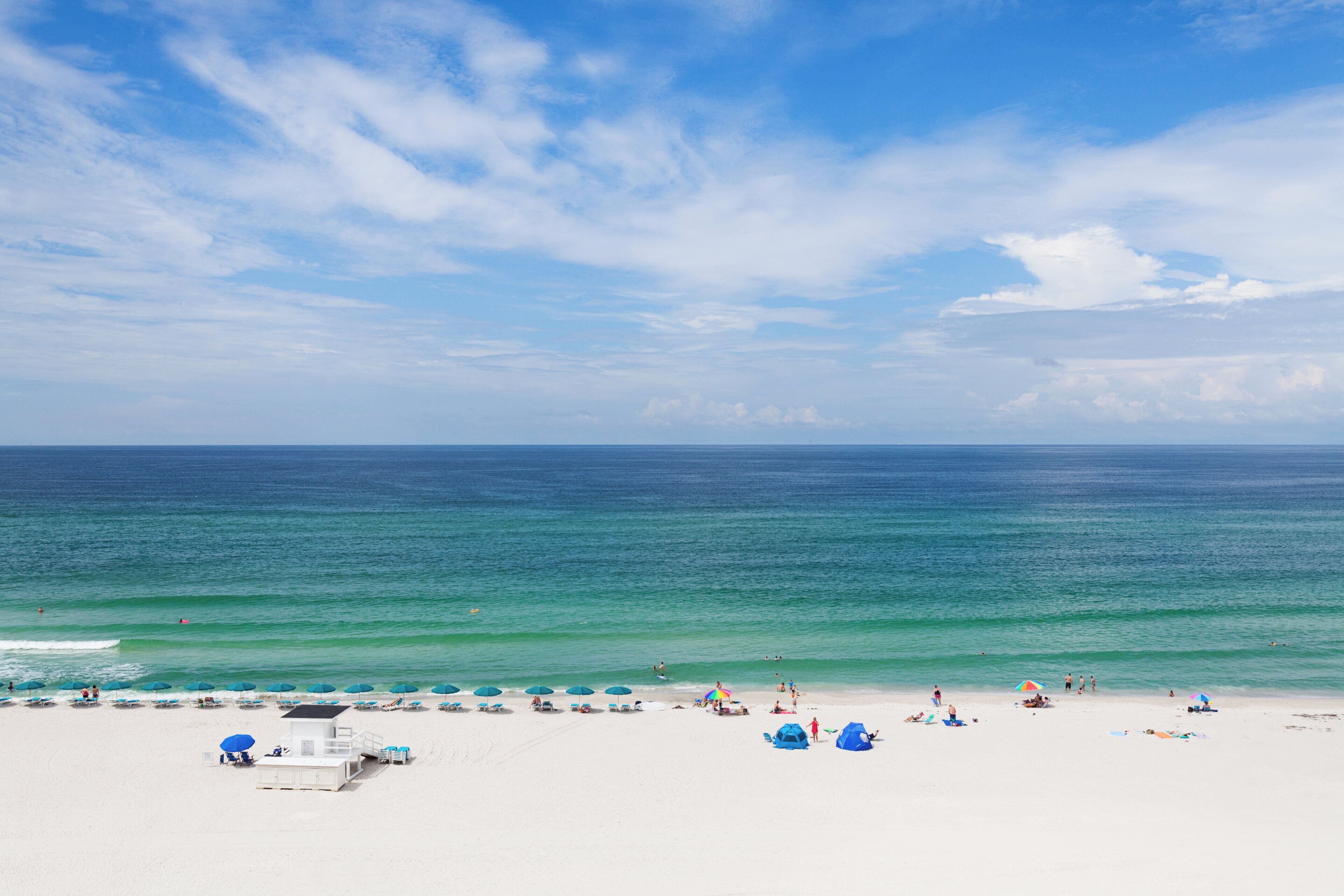 A beach with white sand, a lifeguard tower, and umbrellas.