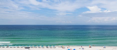 A beach with white sand, a lifeguard tower, and umbrellas.