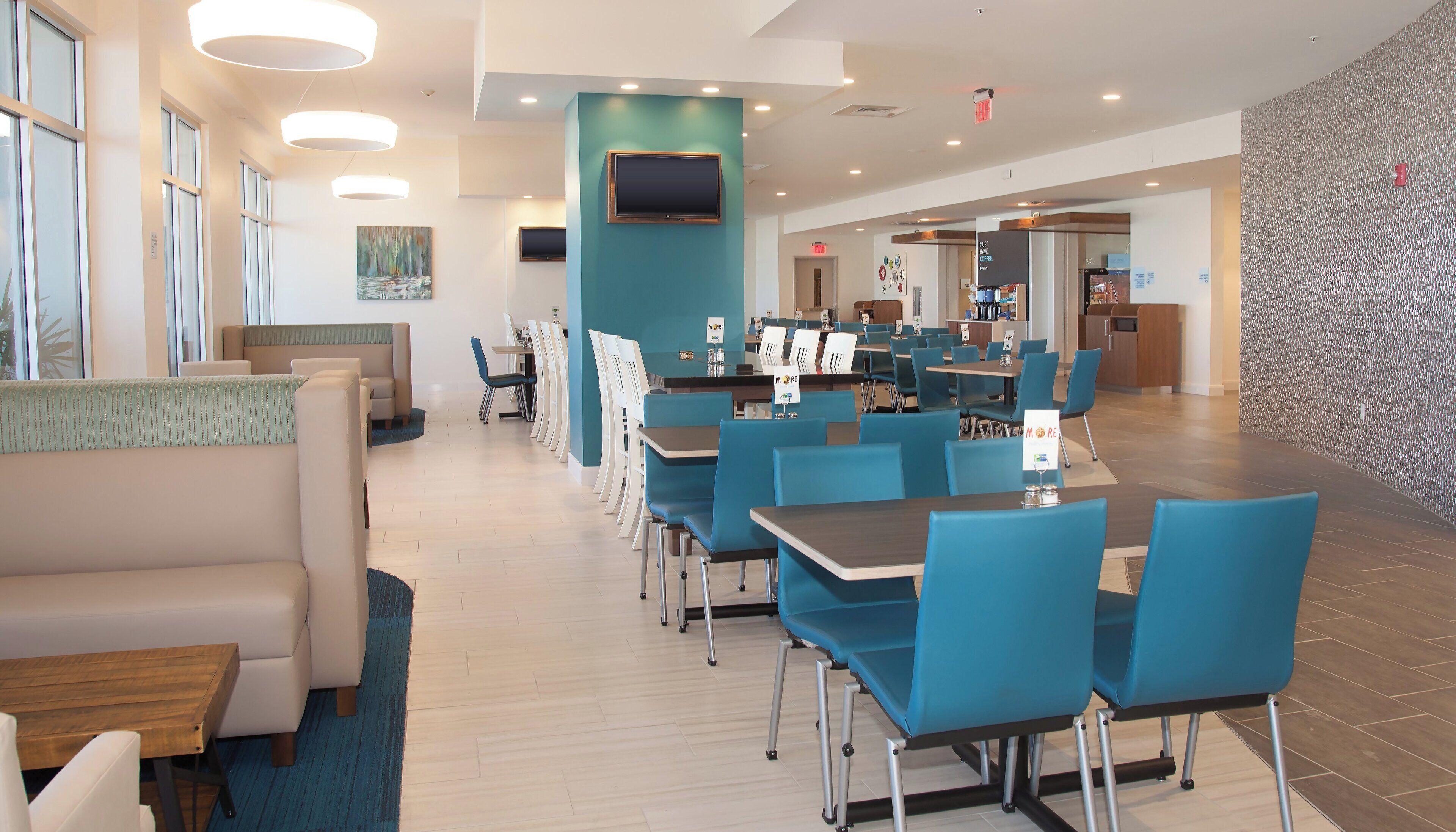 A modern dining area with blue chairs and tables, a flat-screen TV, and a coffee station.
