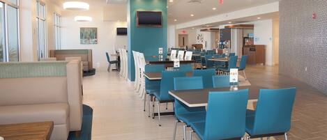 A modern dining area with blue chairs and tables, a flat-screen TV, and a coffee station.