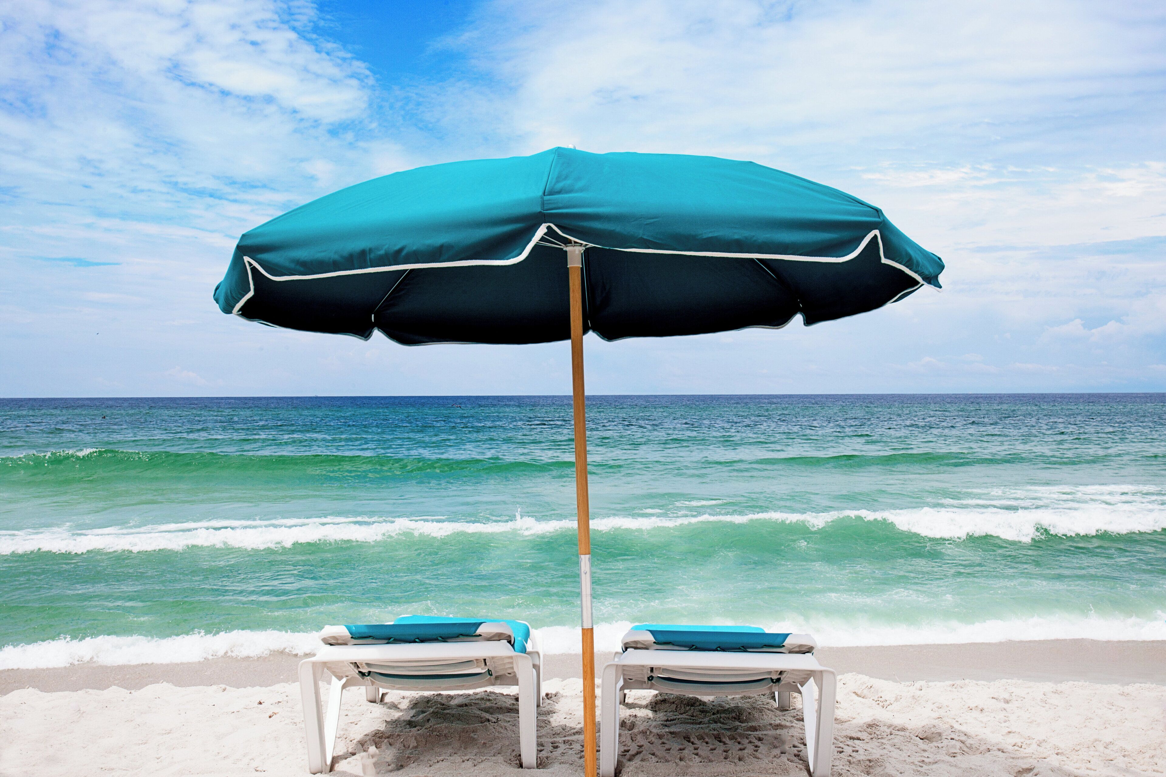 A beach scene with a single umbrella and two lounge chairs.