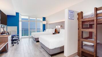 A hotel room with two beds, a desk, and a TV. There is a sign on the wall and a window with blinds.