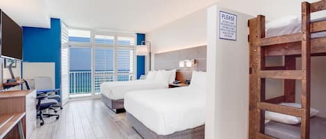 A hotel room with two beds, a desk, and a TV. There is a sign on the wall and a window with blinds.