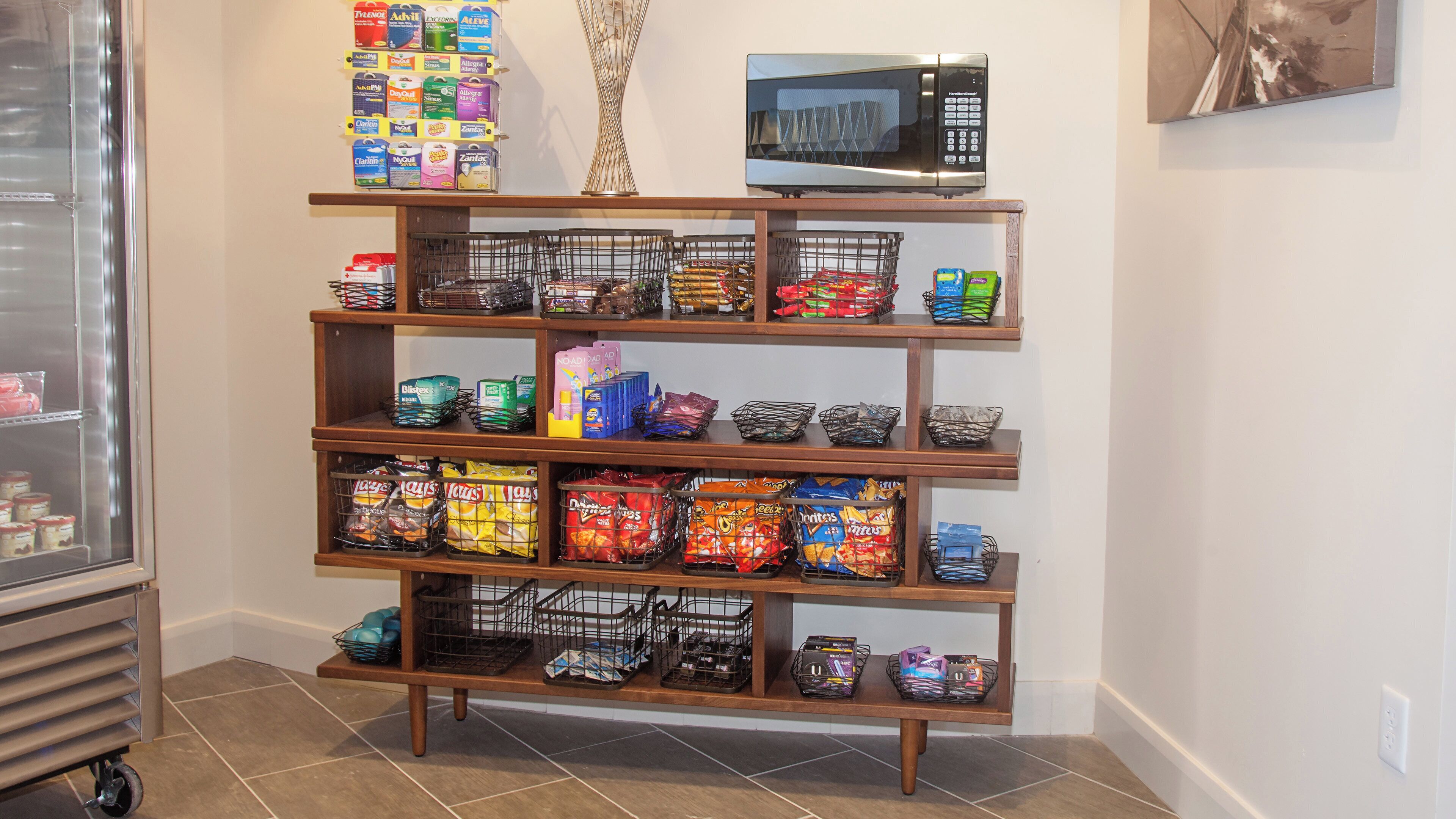 A multi-tiered metal shelf unit with various snack items and a microwave on top.