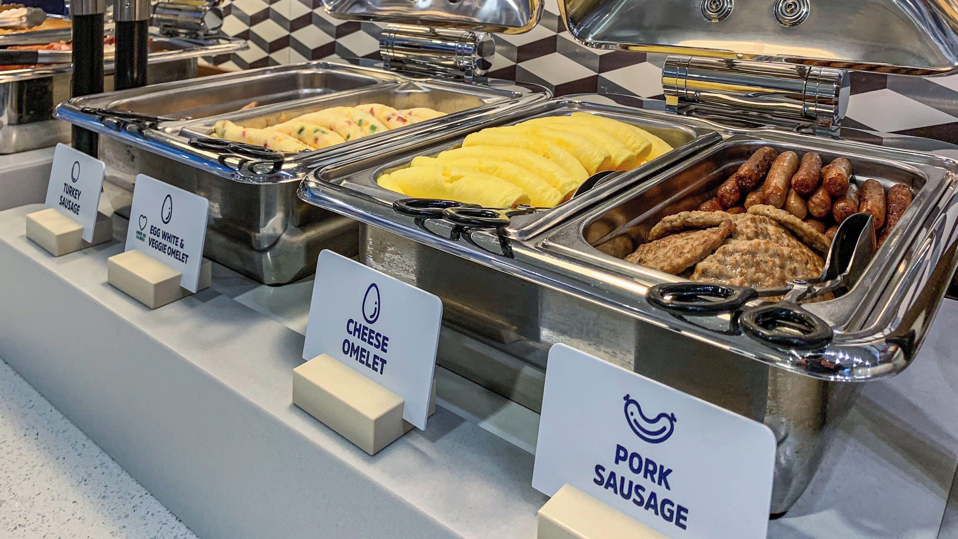 Un buffet proposant différentes sections clairement identifiées, avec notamment des saucisses de dinde, des omelettes aux blancs d’œufs et aux légumes, des omelettes au fromage et des saucisses de porc.