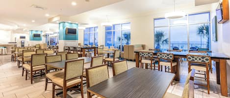 A spacious dining area with multiple tables and chairs, large windows offering views, and a counter with a cash register.