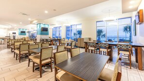 A spacious dining area with multiple tables and chairs, large windows offering views, and a counter with a cash register. - Holiday Inn Express & Suites Panama City Beach - Beachfront by IHG (Panama City Beach)