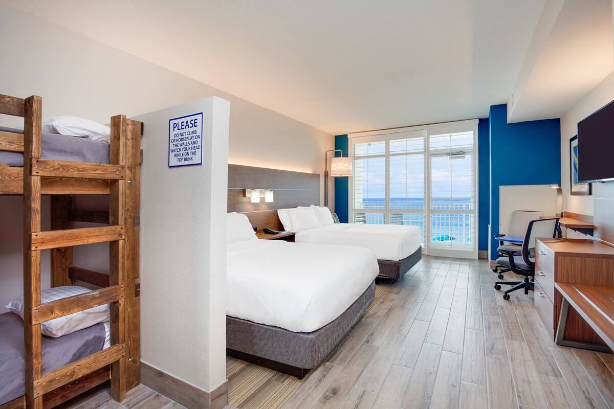 Une chambre d’hôtel avec deux lits, un bureau, une chaise, une télévision et un balcon avec vue.
