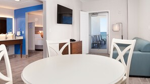 A modern hotel room with a dining area, a balcony with chairs, and a bed with a nightstand. - Holiday Inn Express & Suites Panama City Beach - Beachfront by IHG (Panama City Beach)