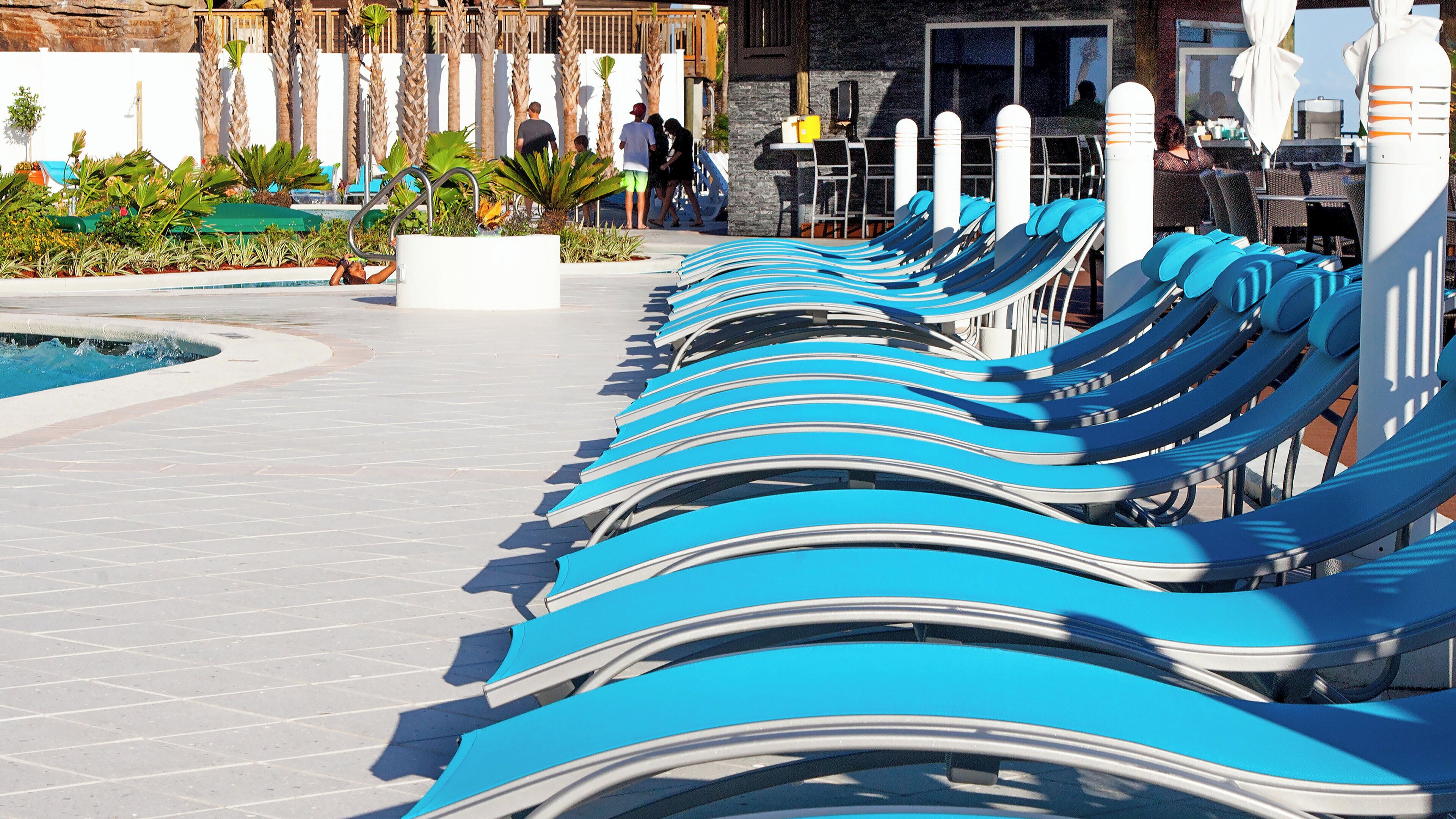 Eine Reihe von Liegestühlen am Pool, mit einem Steinweg und Palmen im Hintergrund.