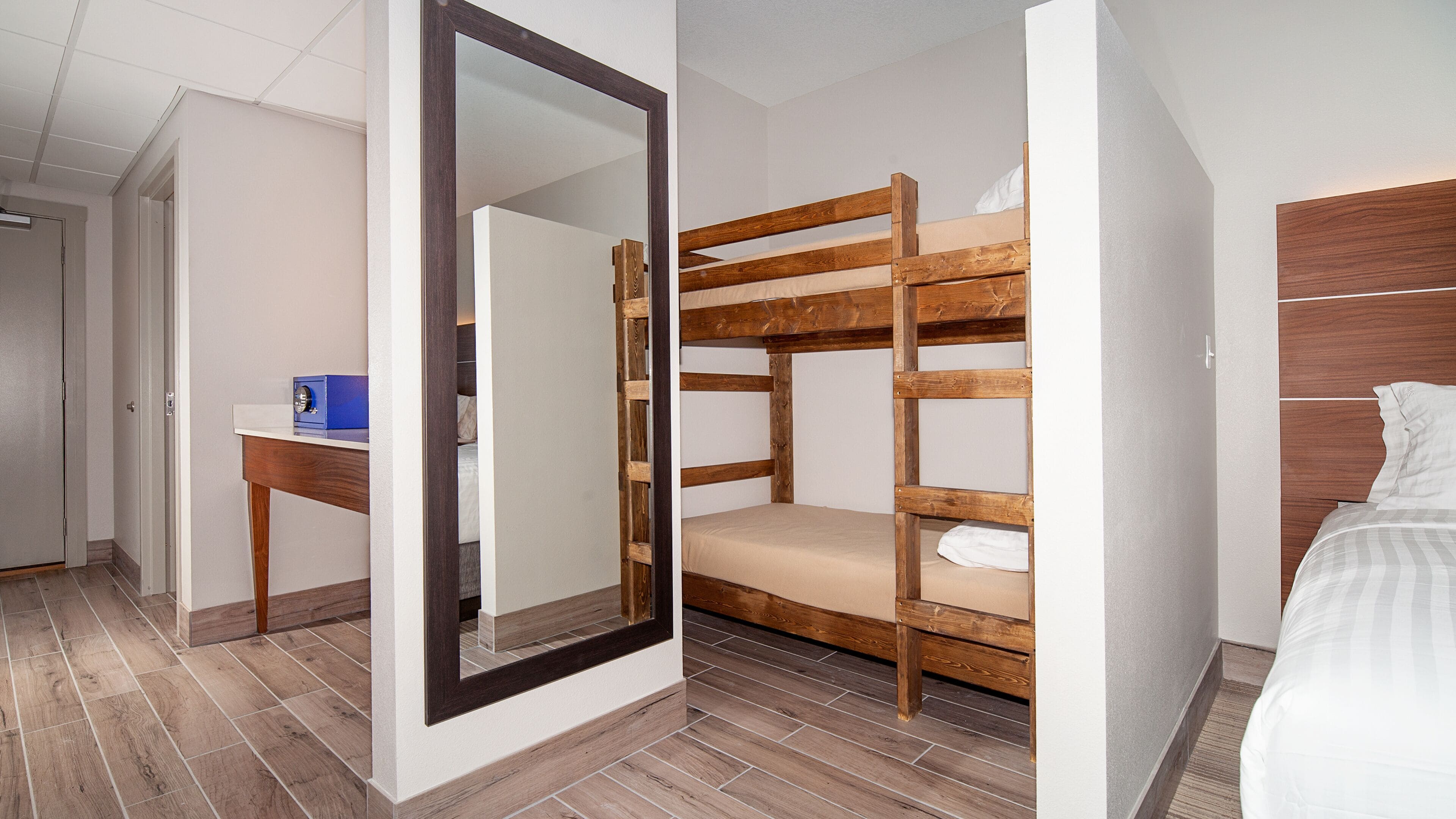 Une chambre d’hôtel avec un lit superposé, un bureau sur lequel se trouve un objet bleu et un grand miroir.