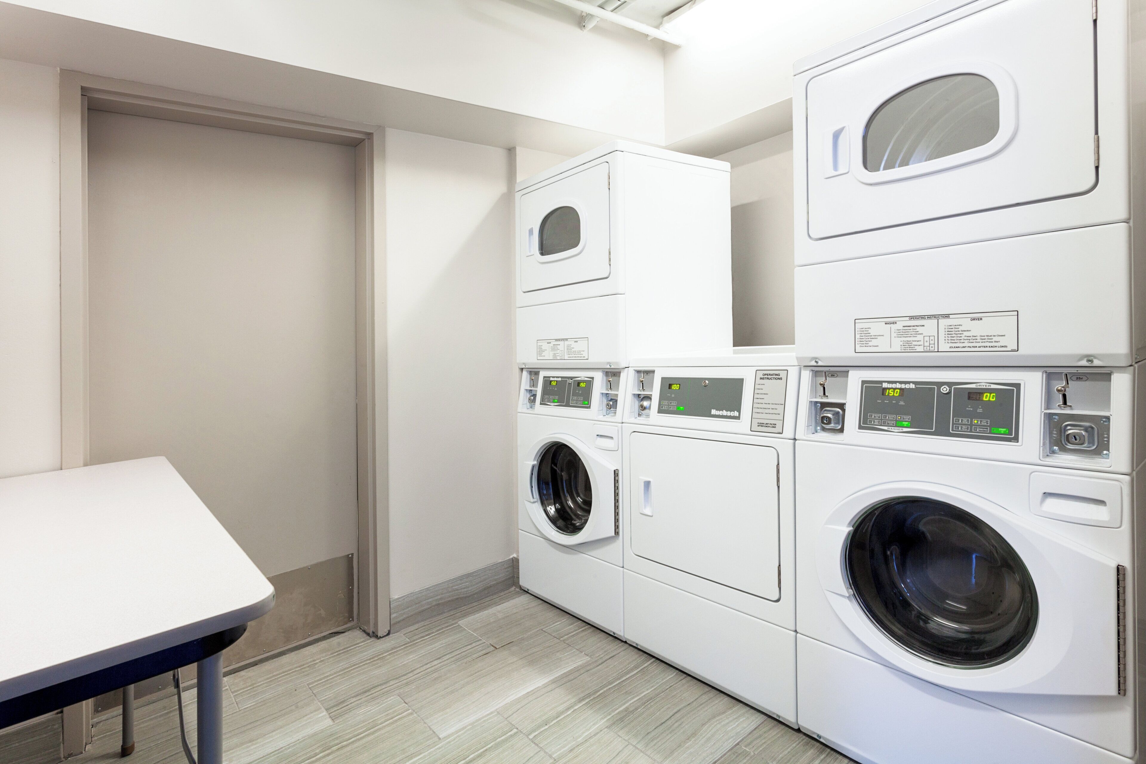A laundry room with a table, a front-loading washer, a top-loading dryer, and a stacked washer and dryer unit.