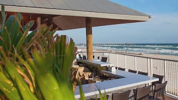 A beachside bar with outdoor seating, overlooking the ocean and a pier.
