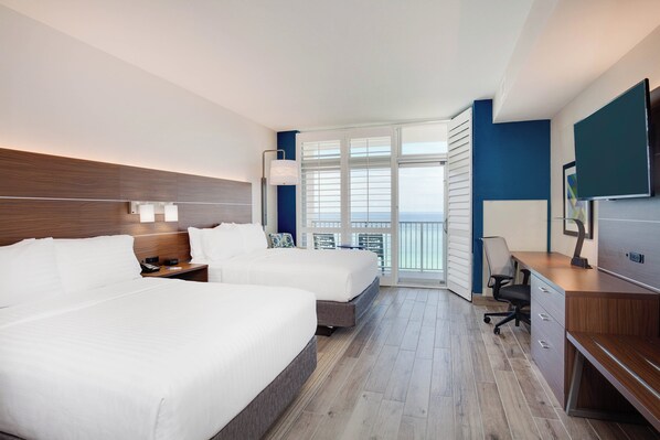 A hotel room with two beds, a desk, a chair, and a large window offering a view of the ocean. - Holiday Inn Express & Suites Panama City Beach - Beachfront by IHG (Panama City Beach)