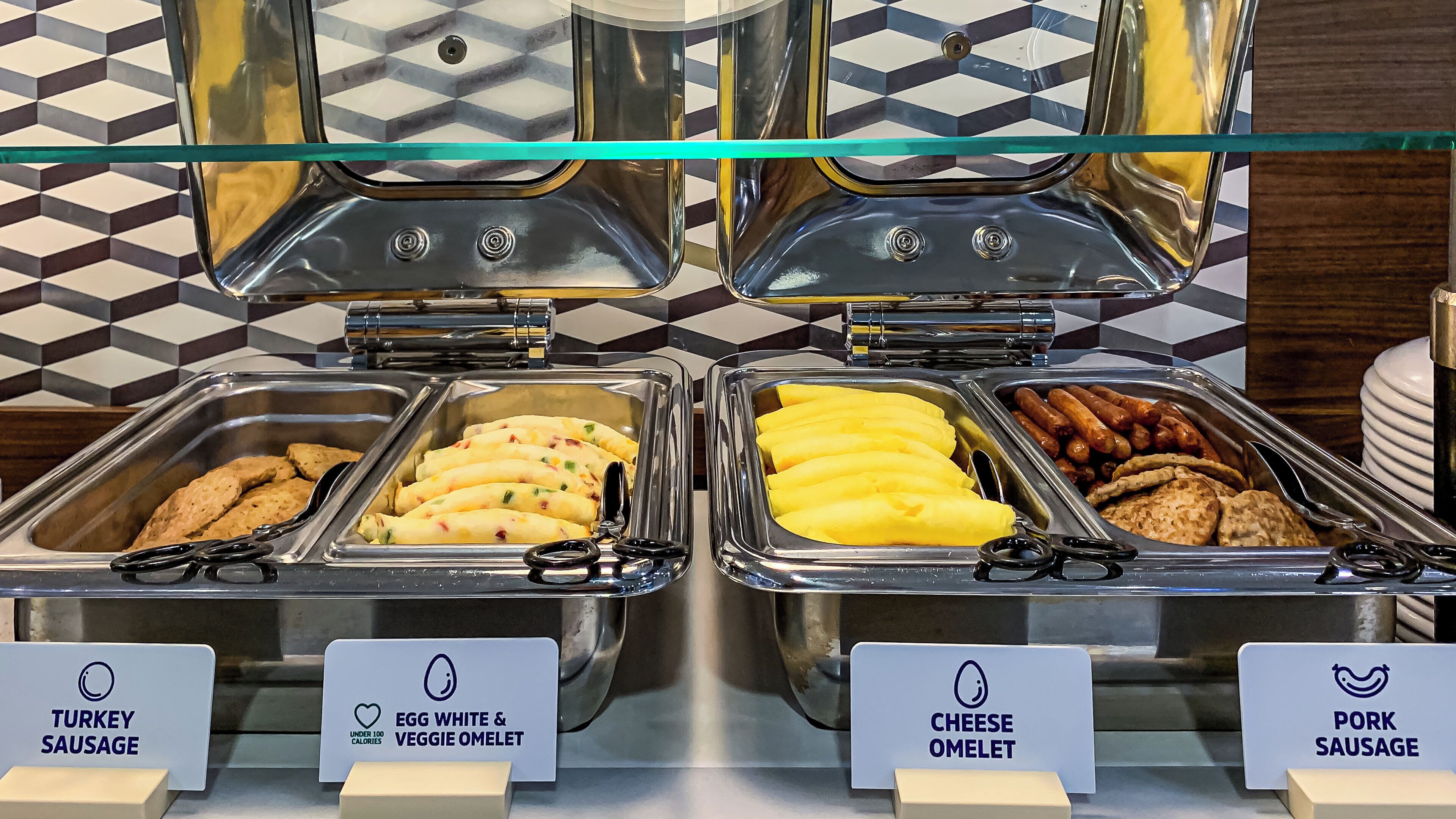 A buffet with labeled sections for turkey sausage, egg white & veggie omelet, cheese omelet, and pork sausage.