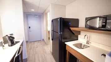 Una cocina compacta con un refrigerador negro, un microondas, un lavamanos y una cafetera.