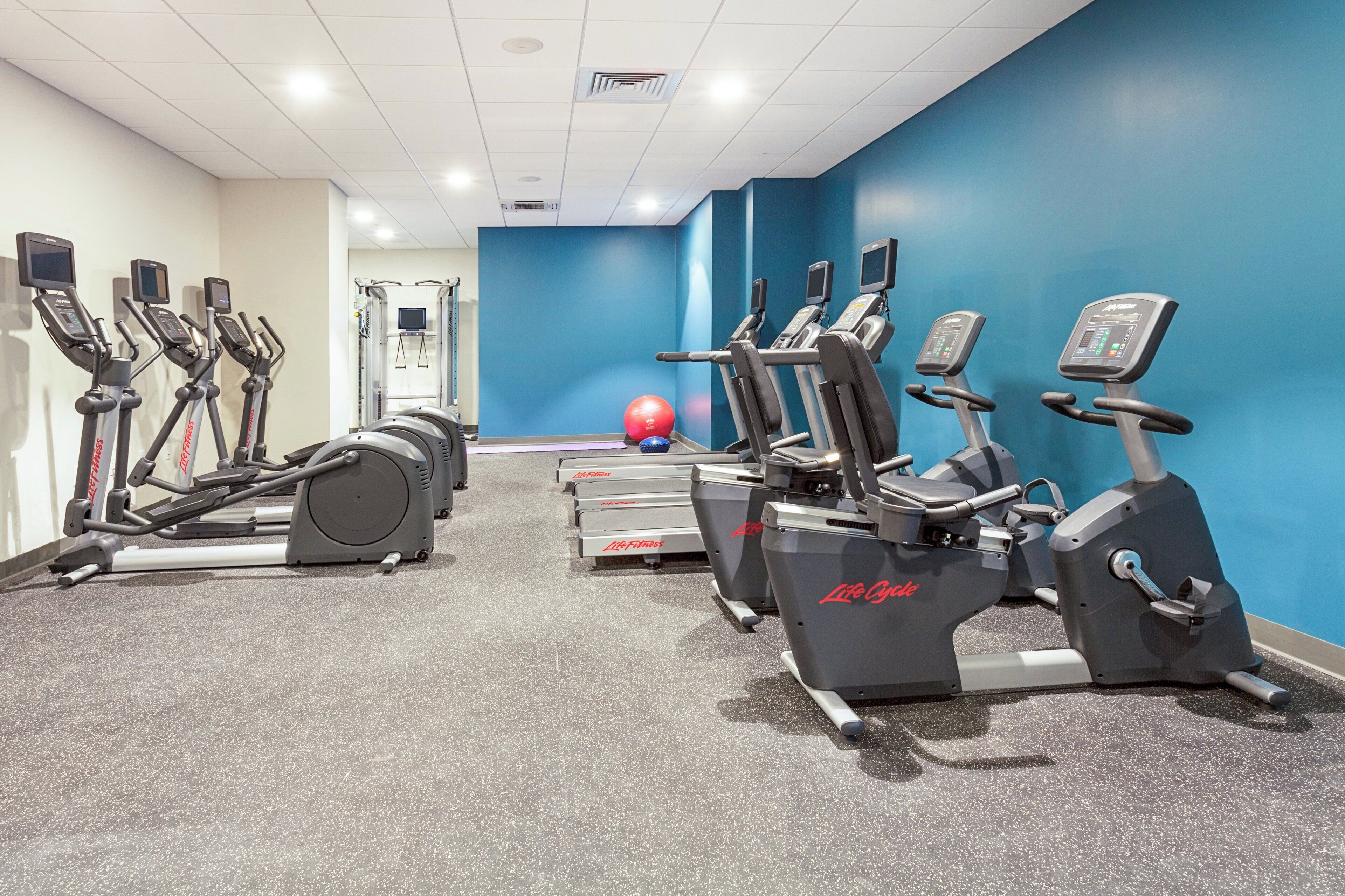 A gym with multiple cardio machines, a rowing machine, and a medicine ball.