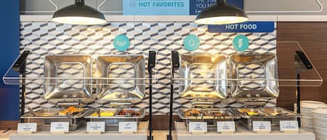 Een buffet met aangeduide secties voor diverse gerechten, waaronder worstsaus, ontbijtkoekjes, roerei, spek, varkensworst, kalkoenworst, kaasomelet en een omelet met eiwit en groenten.