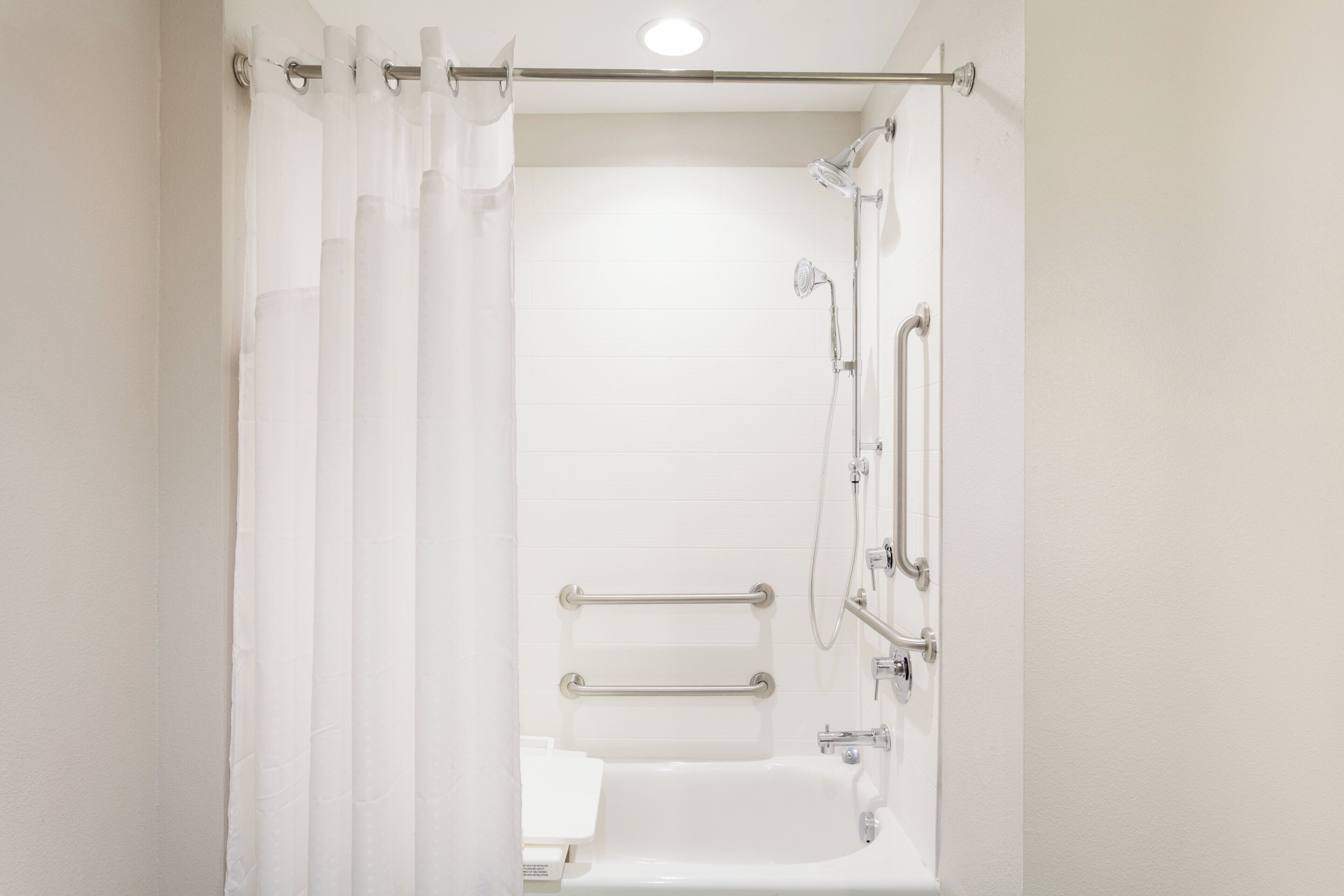 A bathroom with a bathtub, shower, and grab bars.