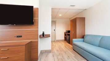 A modern living room with a flat-screen TV mounted on a wooden cabinet, a blue sofa, and a coffee machine on a small shelf.