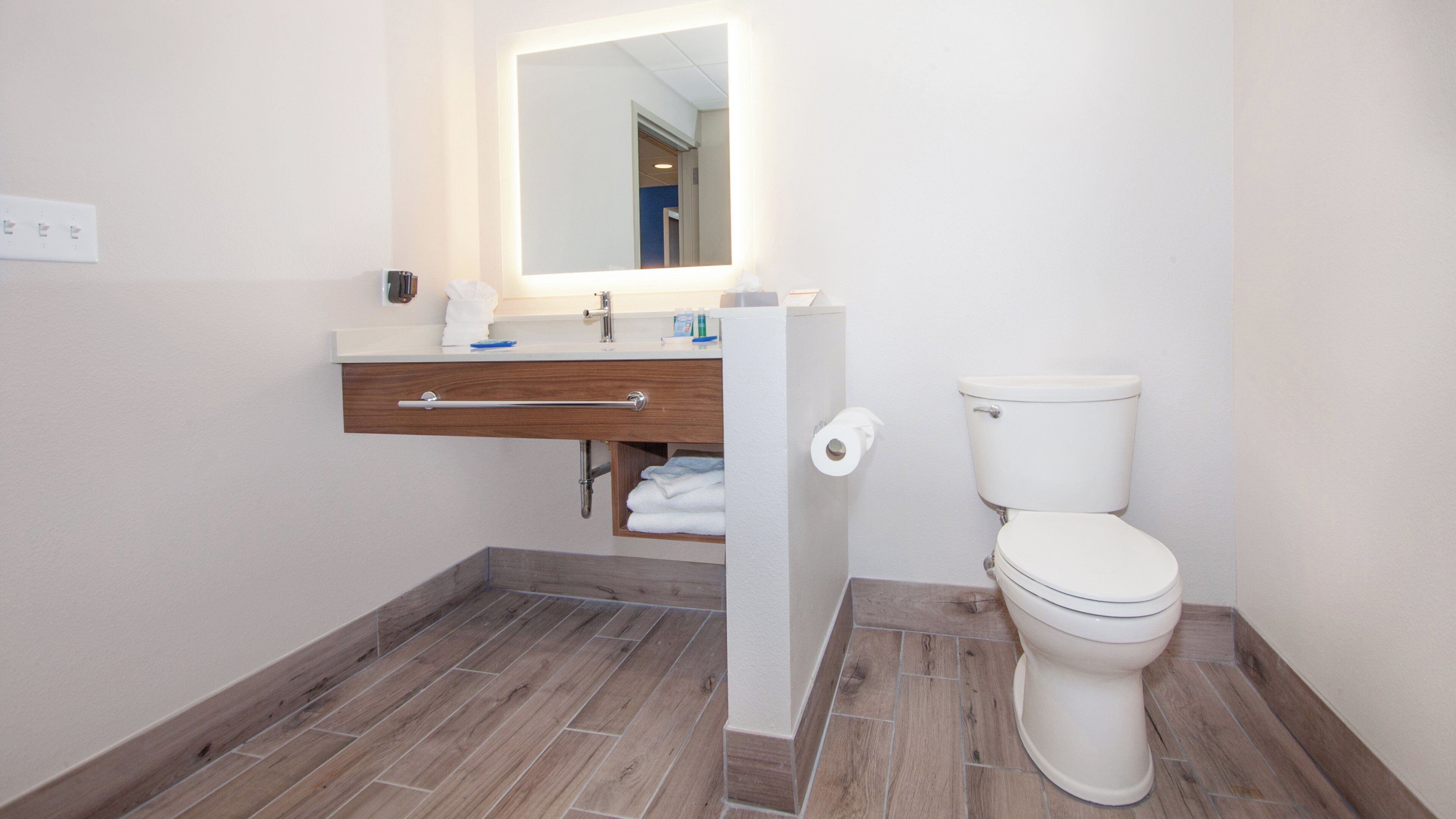 Un baño con inodoro blanco, tocador de madera con espejo y un perchero.