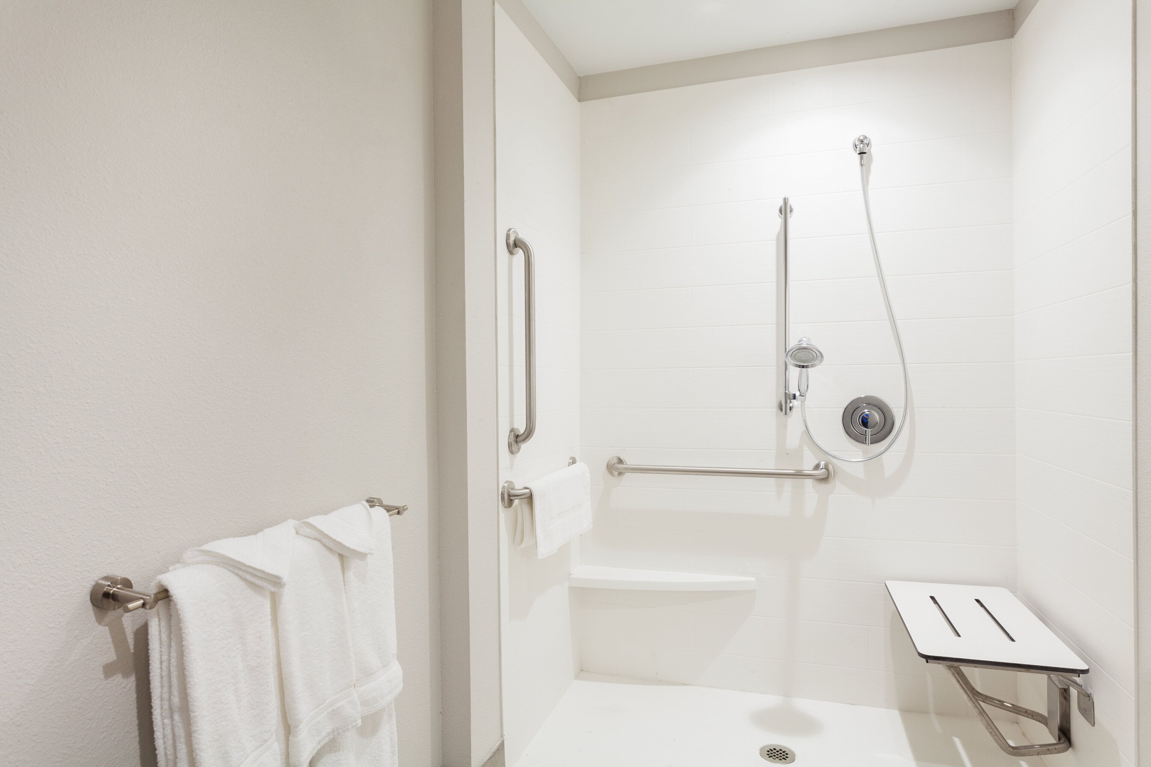 A modern bathroom with a shower, grab bars, and a towel rack.