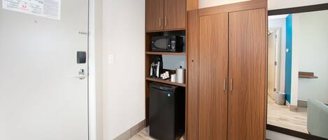 Una kitchenette compacta con microondas, cafetera y refrigerador.