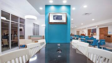 A modern hotel lobby with a central wall-mounted sign, seating areas, and a dining section.