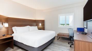 Une chambre d’hôtel moderne, dotée d’un grand lit, d’un bureau avec une chaise, d’une télévision et d’une fenêtre avec des stores.