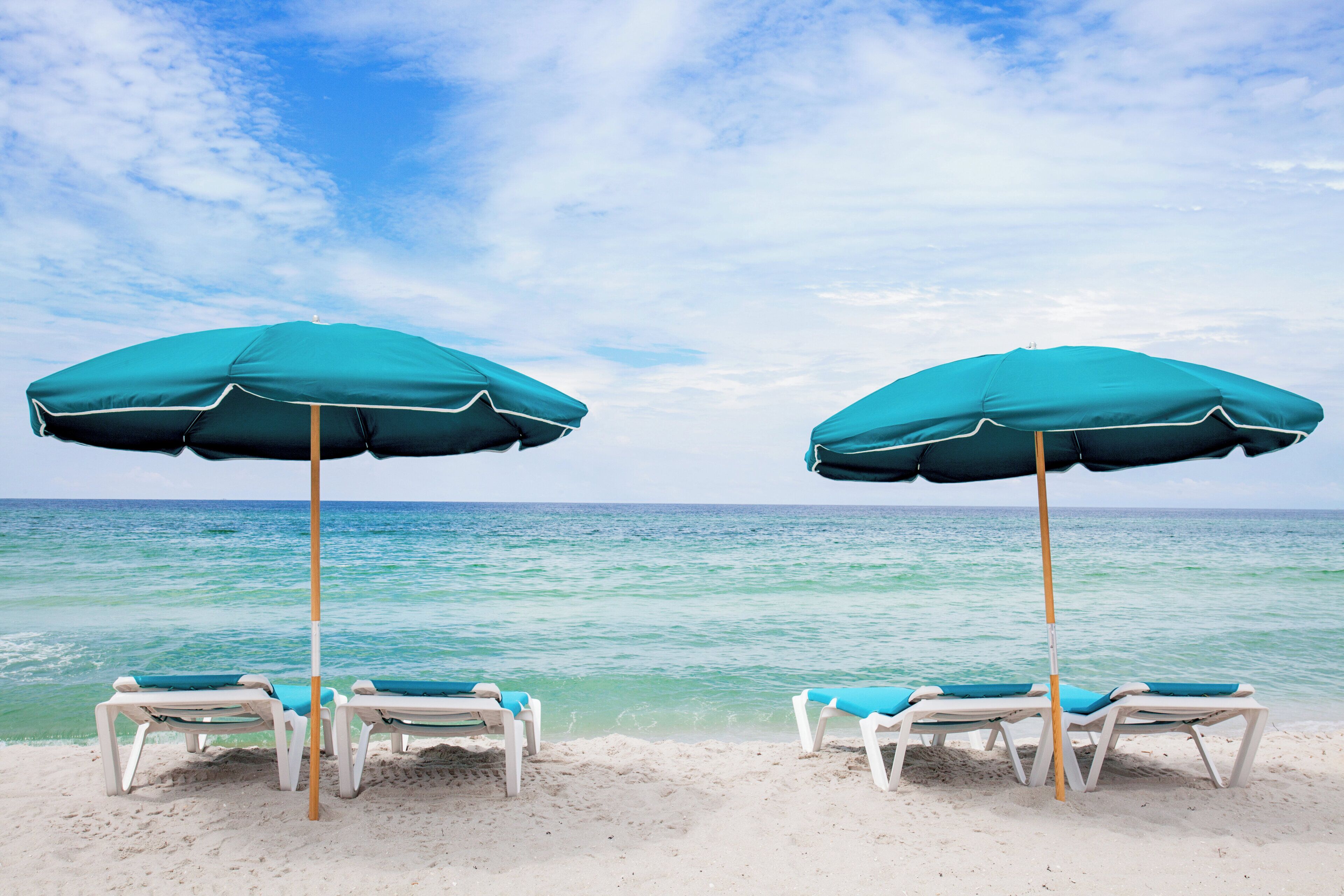 Twee strandparasols en ligstoelen op een zandstrand, met de oceaan op de achtergrond.