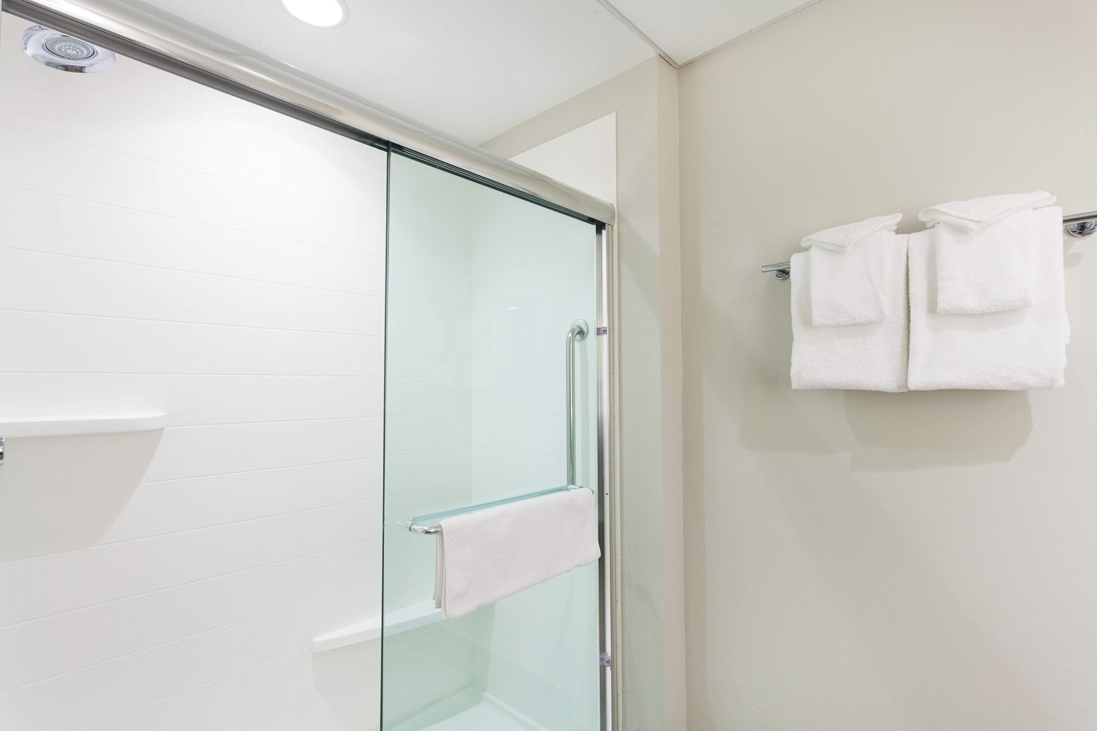 A modern bathroom with a glass shower enclosure, a white towel rack, and a white towel hanging on the wall.